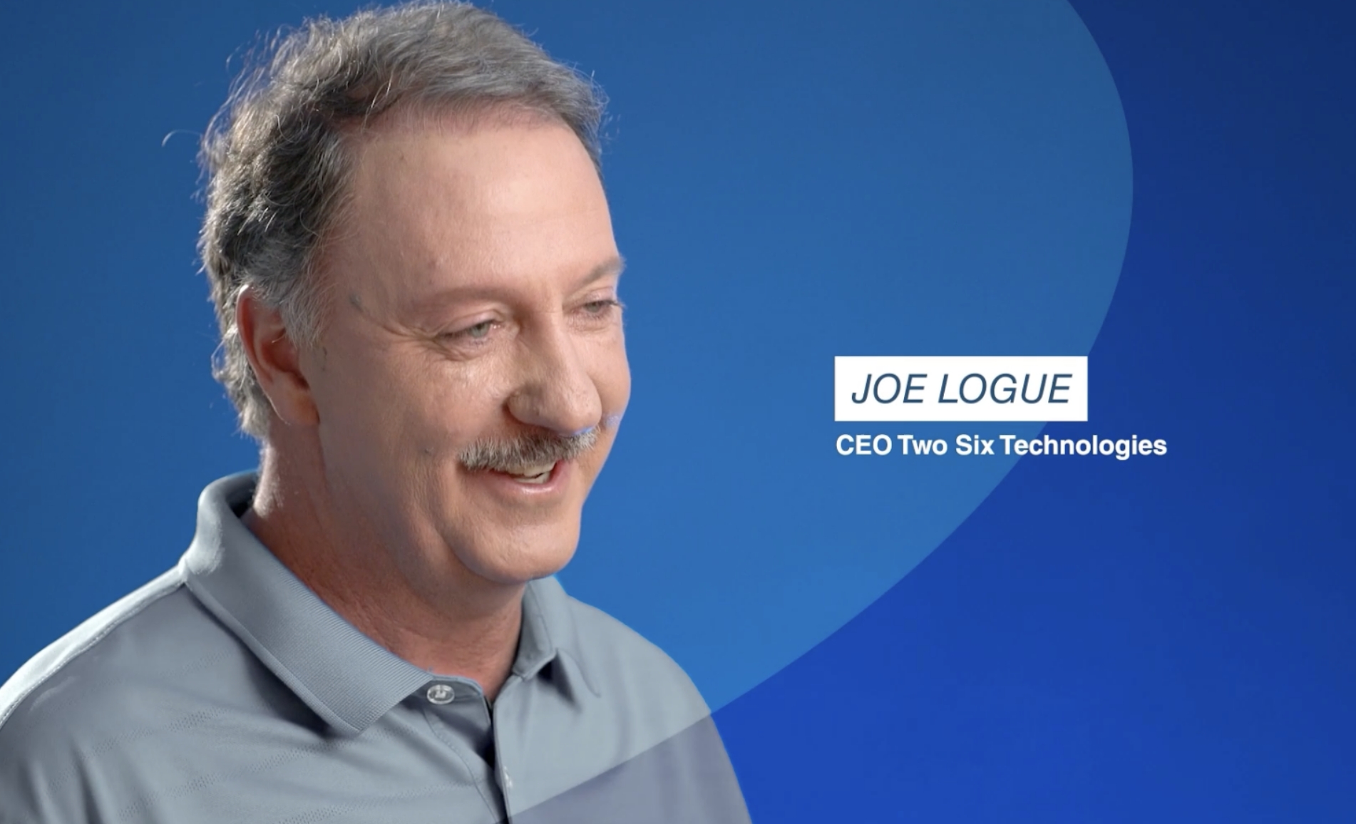 TST-Joe-Logue-Video Joe Logue, CEO of Two Six Technologies, smiling in a professional interview against a blue background.