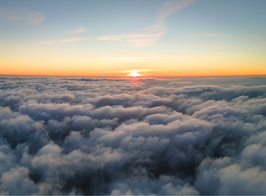 A sunrise over a sea of clouds with a soft, colorful sky and the sun just beginning to rise on the horizon.
